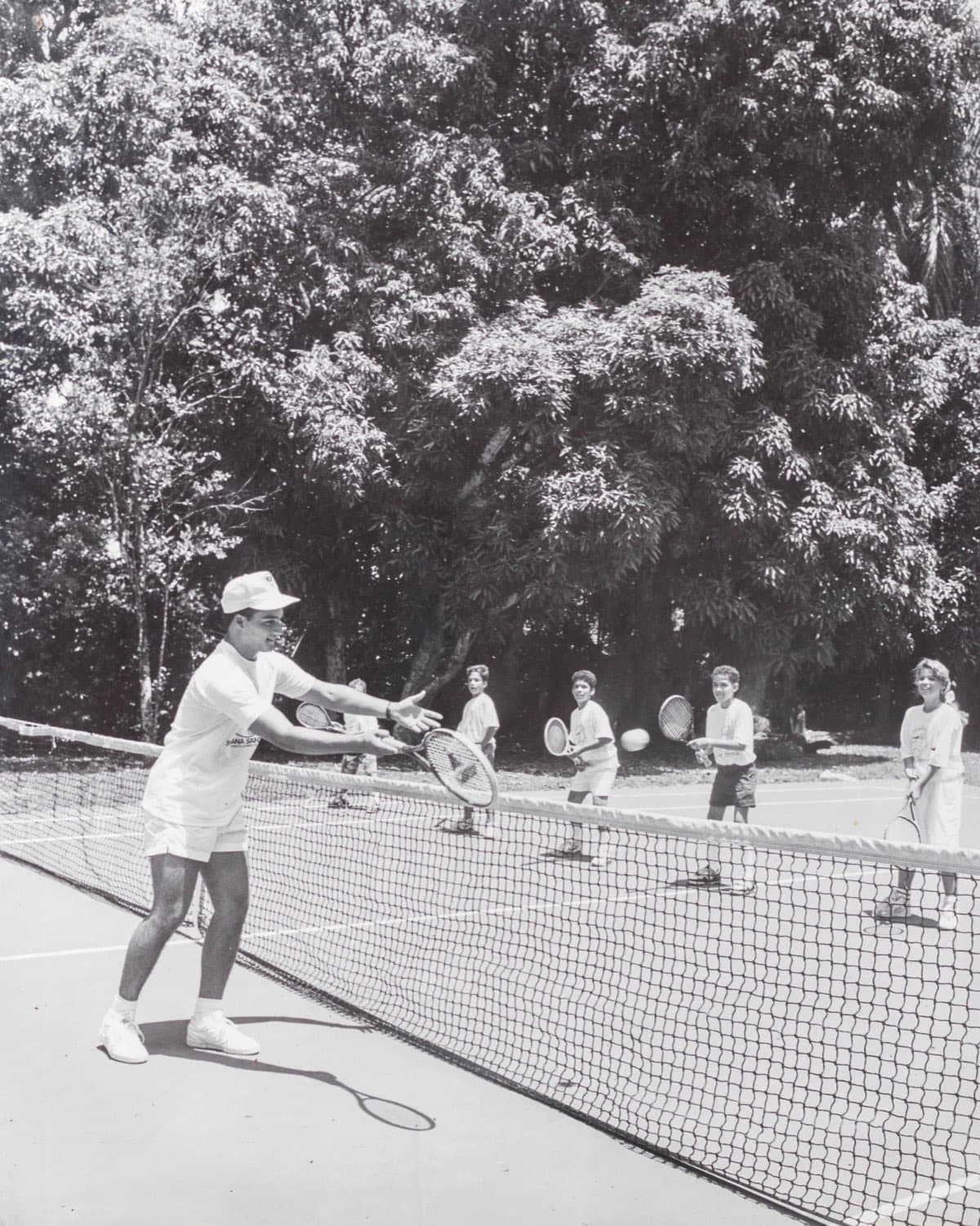 Clase de tenis en Comatillo: un monitor devuelve la bola y cuatro campistas esperan al otro lado de la red